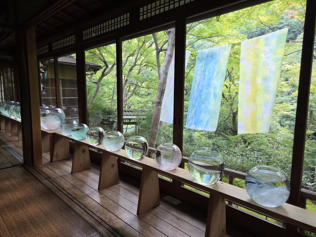 京都・嵐山祐斎亭の水鏡展示。丸いガラス鉢に庭園の景色が映り込み、色彩豊かな染色作品が窓辺を彩る。